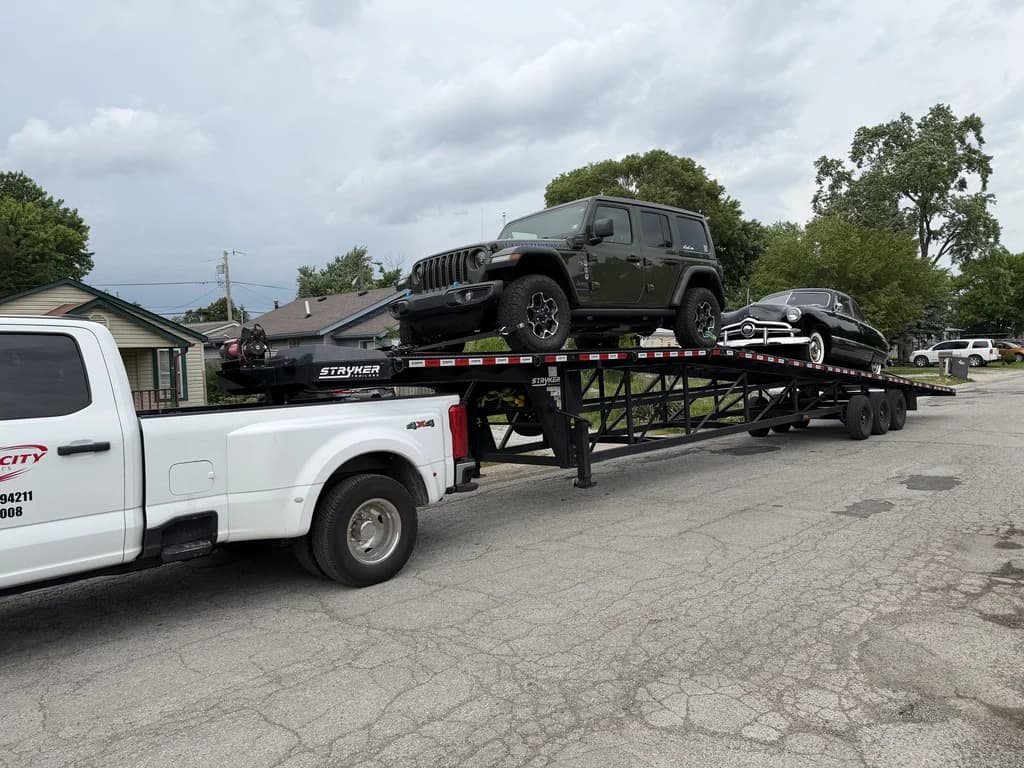 A Velocity Logistics truck and wedge carrier loaded with a Jeep and a classic car on a residential street