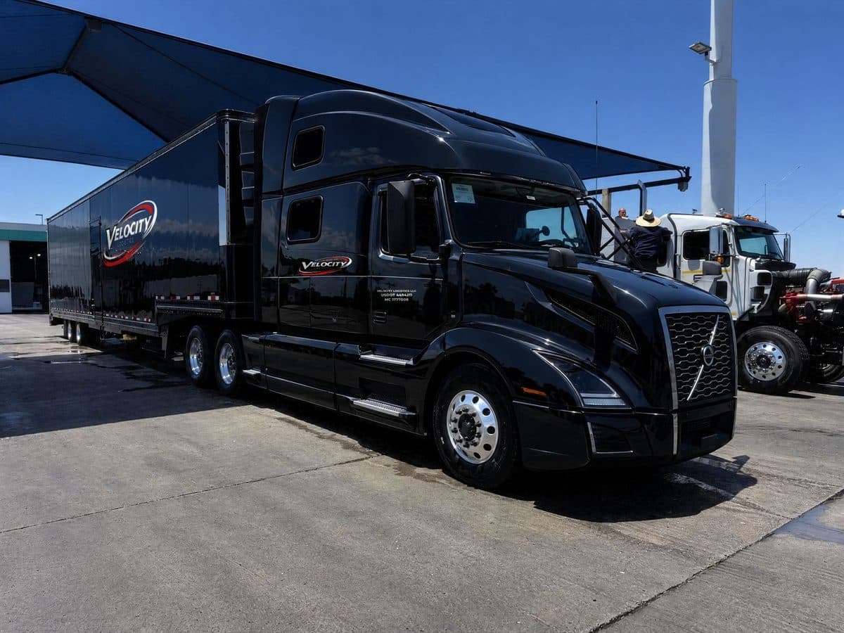 Black Velocity Logistics Volvo semi with an enclosed car trailer, logo, USDOT and MC on the cab