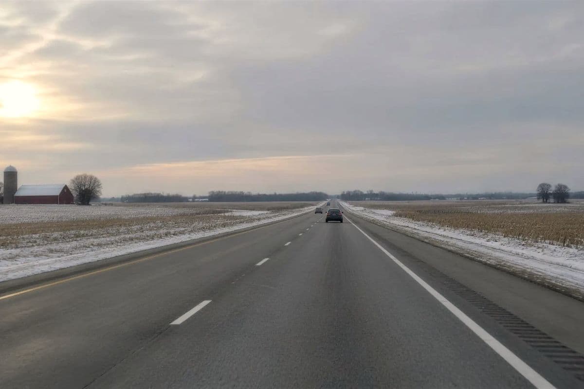 Straight interstate through snow-dusted farm fields, a red barn and silo far off