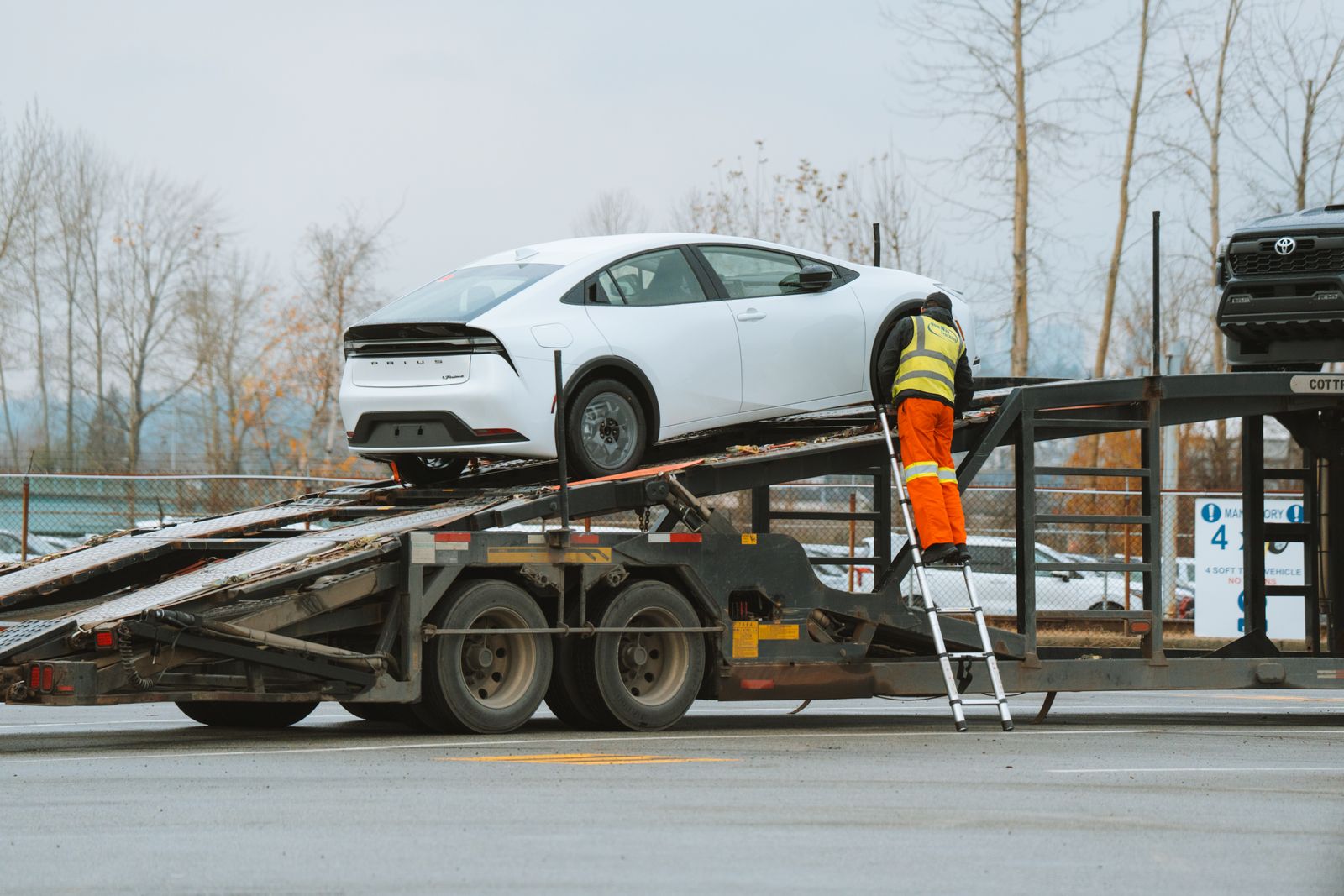 A carrier driver in high-visibility gear loading a car onto a transport trailer