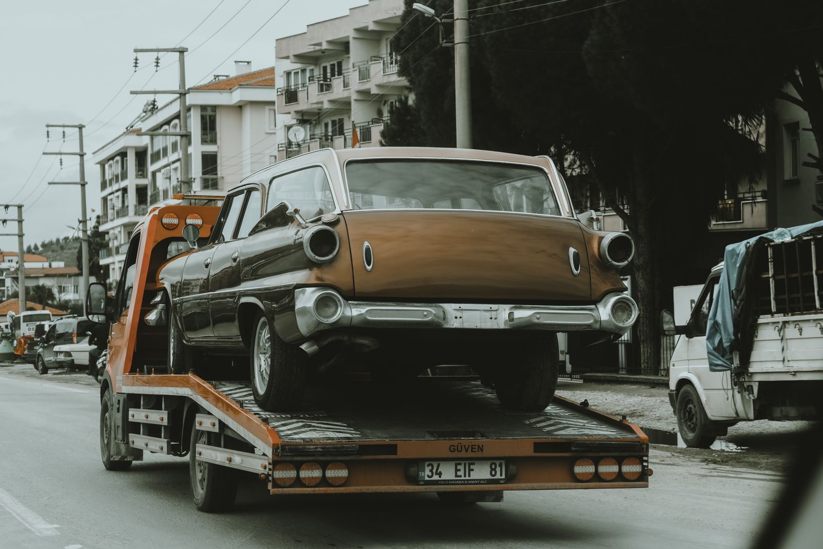 A vintage classic car secured on a flatbed trailer on a city street