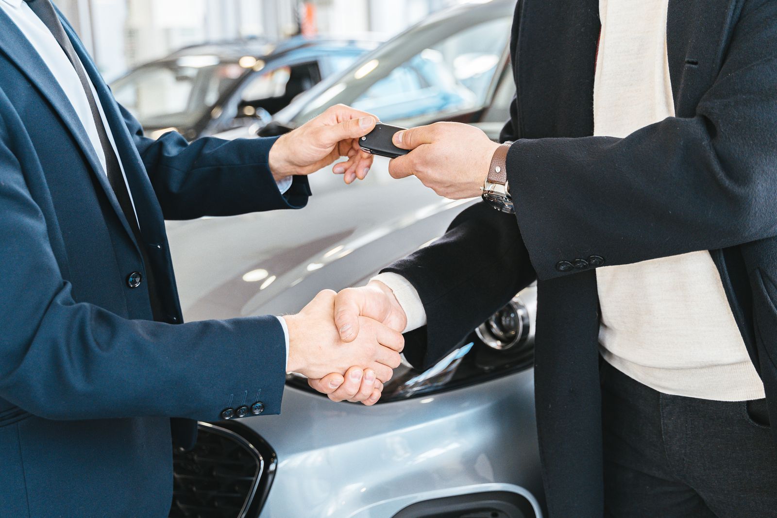 Two people shaking hands as car keys change hands in front of a vehicle