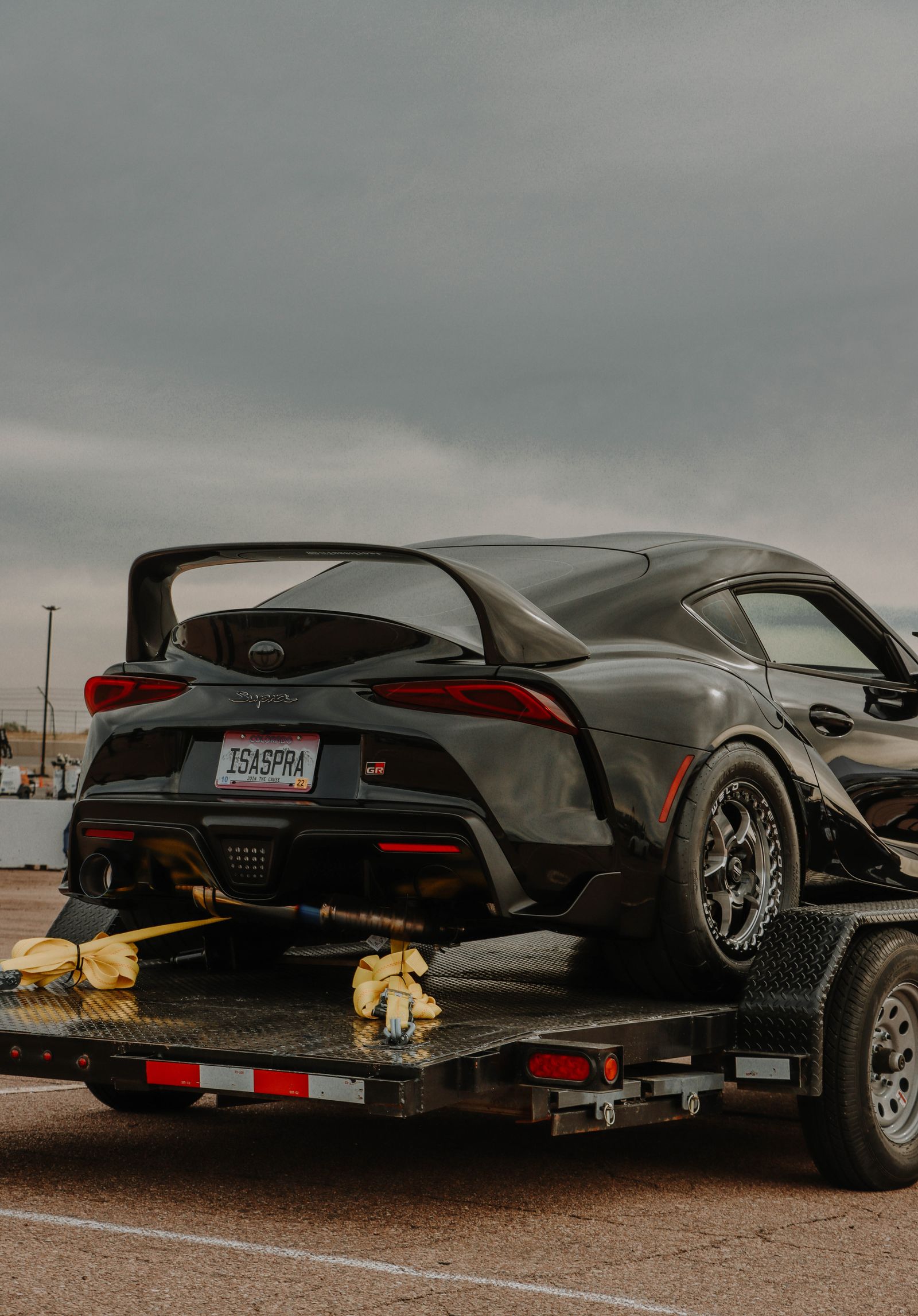 A sports car secured to a trailer by the wheels with soft over-the-tire straps